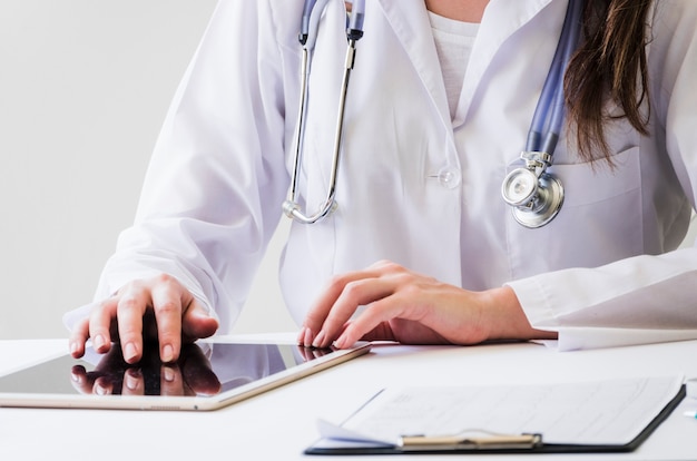 Free photo close-up of a female doctor using digital tablet and medical report on desk