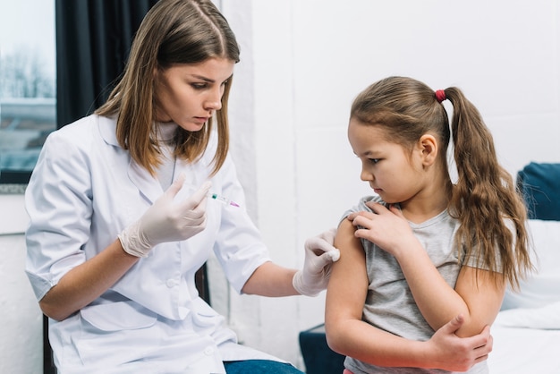 Close-up of female doctor wearing white gloves in hand giving the syringe on patient's arm