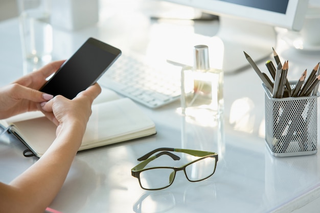 Close-up of female hands using phone while working on computer at modern office interior