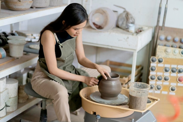 Close up of female hands working on potters wheelasian female sculpture woman shaping mold small vase bowl clay on potter's wheel at home studio workshop art and creation hobby concept