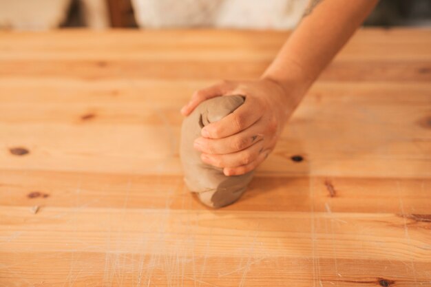 Close-up of female potter's hand kneading the clay on wooden surface