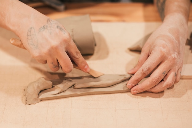 Close-up of female potter's hand molding the wet clay with wooden tools