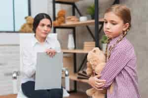 Free photo close-up of female psychologist looking at sad girl holding teddy bear