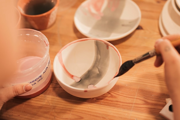 Close-up of female's hand painting the ceramic bowl with paintbrush