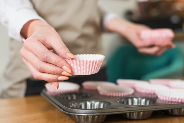 Close-up of female's hand placing paper cups in the muffin pan