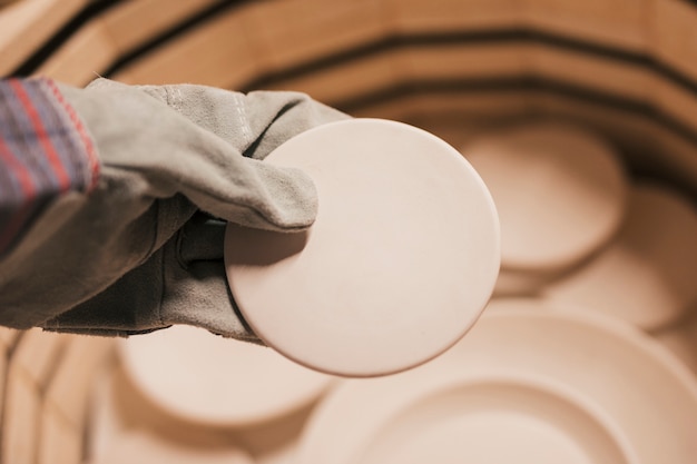 Free Photo close-up of female's hand wearing gloves holding ceramic plates