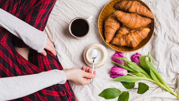 Close-up of female sitting on bed adding powdered milk in the tea cup