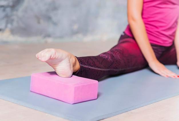 Close-up of a fitness woman stretching her leg using pink yoga block