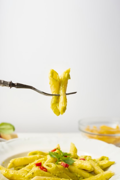 Free Photo close up fork and penne with pesto and red peppers in bowl