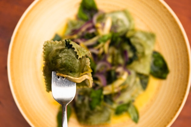 Close-up of fork with green ravioli pasta in plate