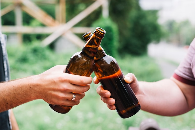 Close-up of friend's hand toasting brown beer bottles at outdoors