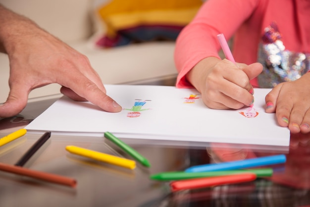 Close-up of girl drawing and her father pointing