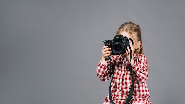 Close-up of a girl holding camera in front of her face standing against gray backdrop