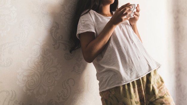 Close-up of a girl holding cup of coffee standing against wallpaper