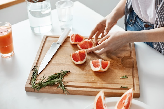 Close up of girl's hands sliced grapefruit knife and rosemary on wooden desk. Copy space.