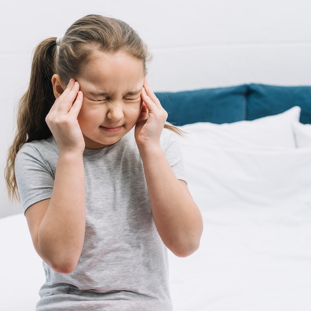 Close-up of a girl sitting on bed having sever pain in headache