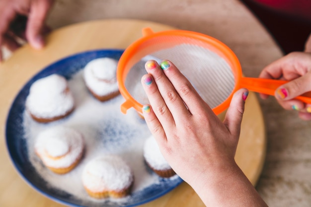 Close-up of girl sprinkling sugar on cupcakes