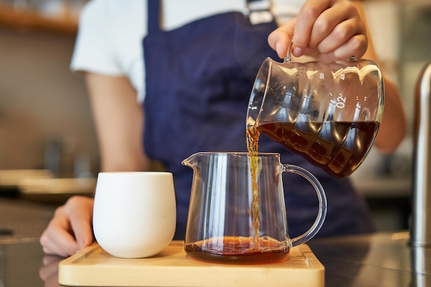 Free photo close up of glass jar and a cup standing on cafe counter barista pouring filter coffee and preparing