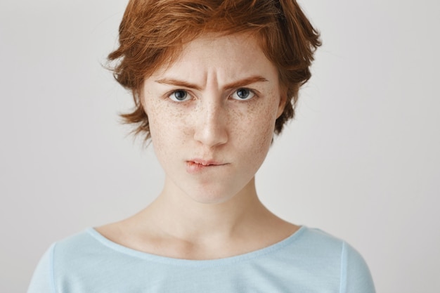 Close-up of gloomy redhead girl posing against the white wall