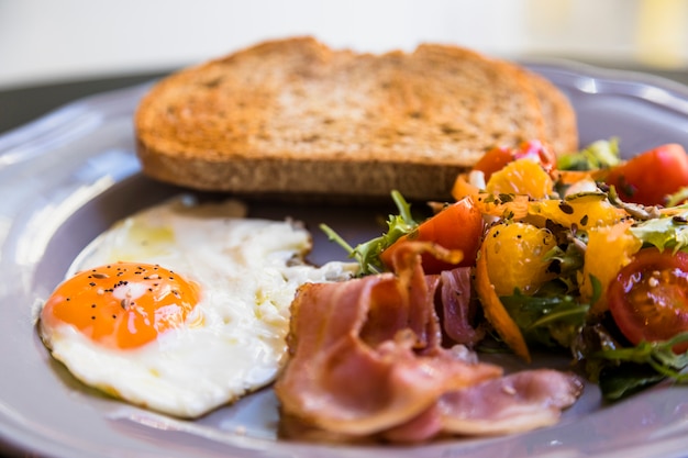 Close-up of gray plate with toast; fried eggs; bacon and salad