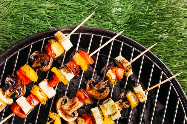 Free photo close-up of grilled skewers with meat and vegetable on grill over green grass mat