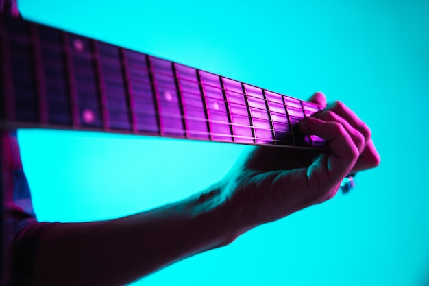 Free photo close up of guitarist hand playing guitar, macro. concept of advertising, hobby, music, festival, entertainment. person improvising inspired. copyspace to insert image or text. colorful neon lighted.