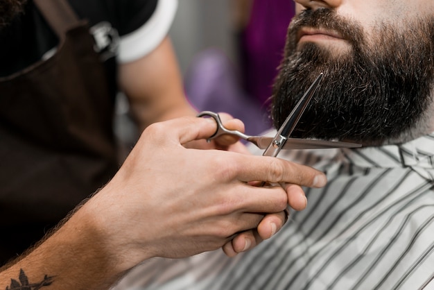 Close-up of a hairdresser's hand cutting man's beard with scissors