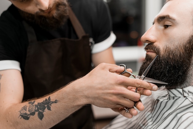 Close-up of a hairstylist's hand cutting man's beard with scissors