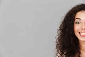 Free photo close up half face portrait of attractive curly woman with ring in nose posing smiling with perfect white teeth over grey wall