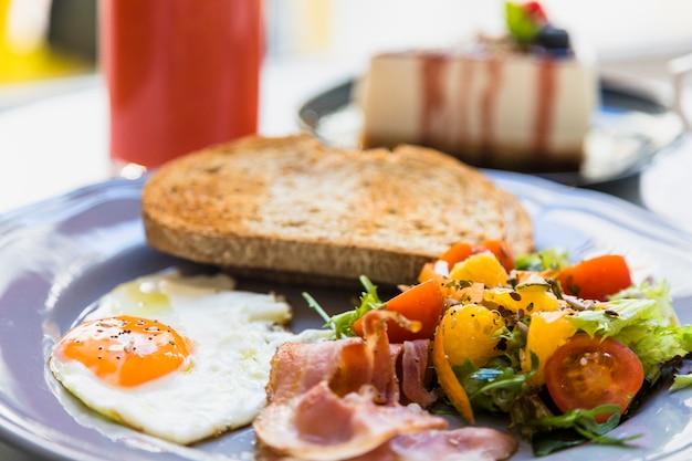 Close-up of half fried egg; bacon; salad and toast on gray ceramic plate