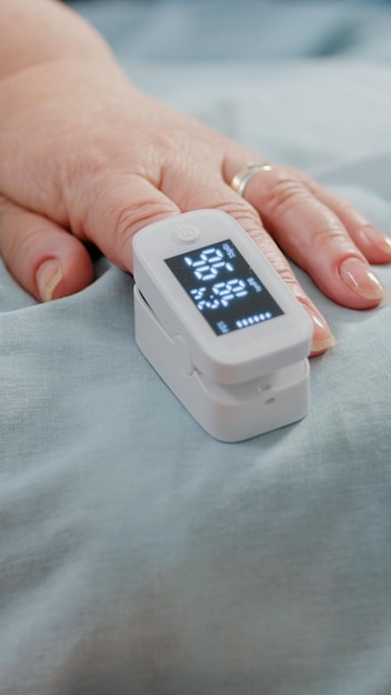 Free Photo close up of hand of aged patient with oximeter in bed. senior person having medical tool on finger for oxygen saturation and pulse pressure measurement. pensioner with sickness