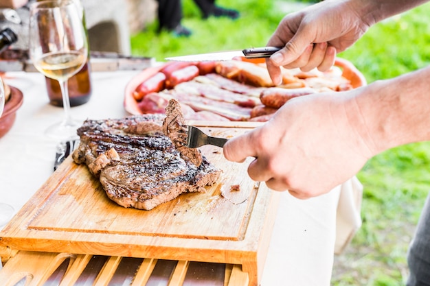 Free photo close-up of hand cutting fresh grilled beef on table at outdoors