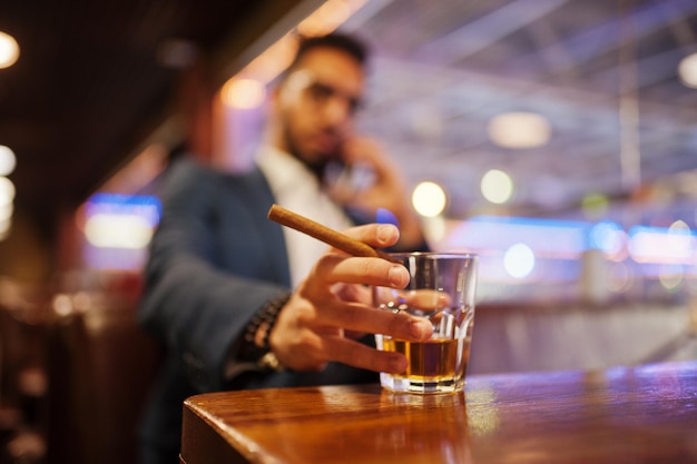 Free photo close up hand of handsome welldressed arabian man with glass of whiskey and cigar posed at pub