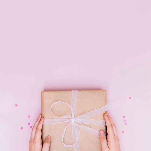 Close-up of hand holding birthday wrapped gift box with white ribbon on pink background