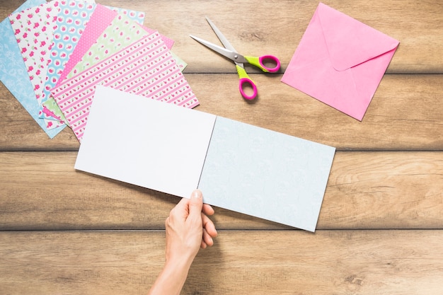 Close-up of hand holding blank card paper against wooden backdrop