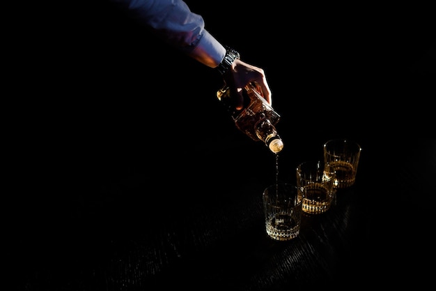 Close up hand holding bottle pours the drink into a glass in black dark space Concept of celebrating and stag party barman cocktails