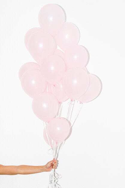 Close-up of hand holding bunch of pink balloons against white backdrop