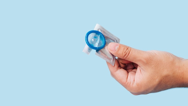 Close-up hand holding condom with blue background