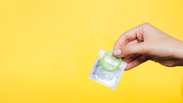 Close-up hand holding a condom with yellow background