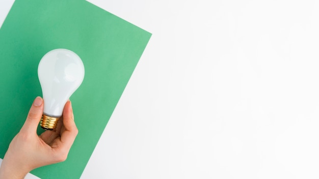 Close-up of hand holding light bulb over green paper against white background