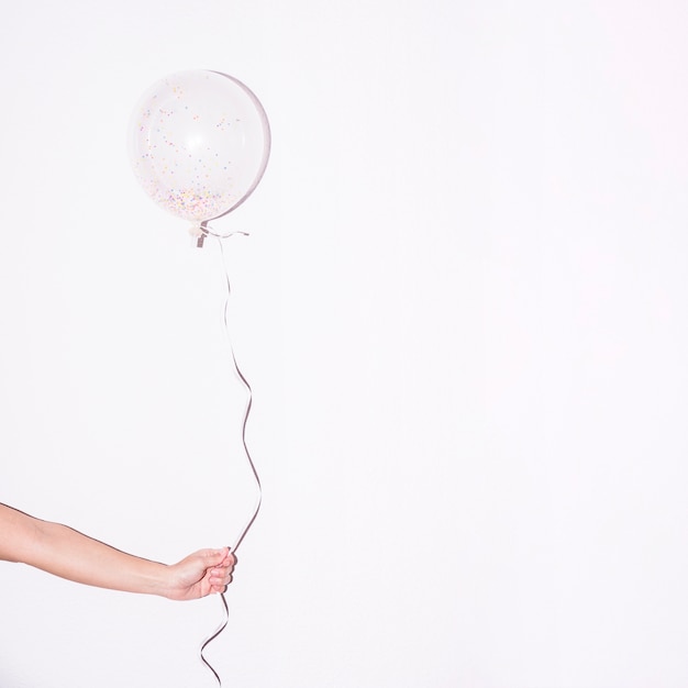 Free Photo close-up of hand holding single white balloon with colorful sprinkle inside it against white backdrop