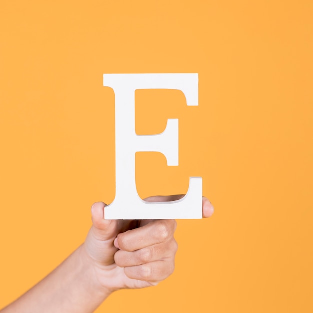 Close-up of hand holding up the uppercase capital letter e over yellow background