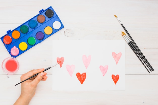 Close-up of hand painting heart shapes with water color on white sheet