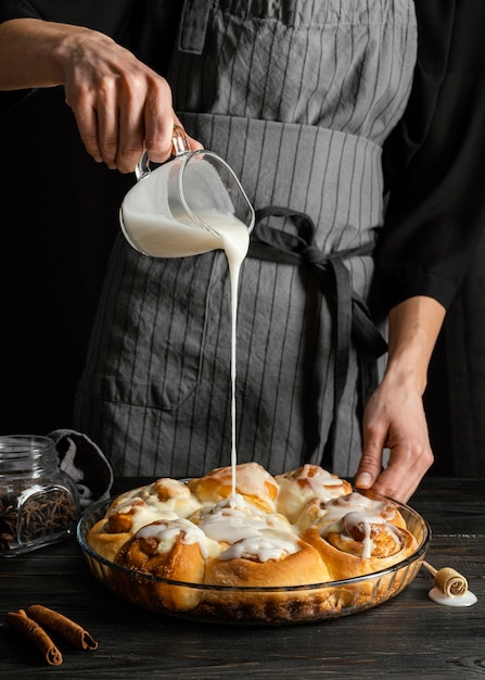 Close up hand pouring cream on cinnamon rolls