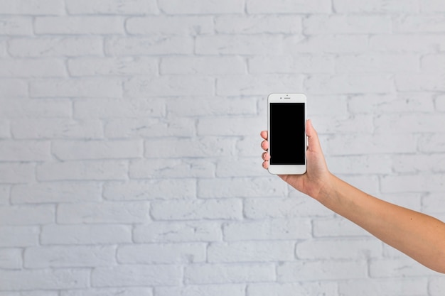 Free photo close-up of hand showing mobile phone in front of white brick wall