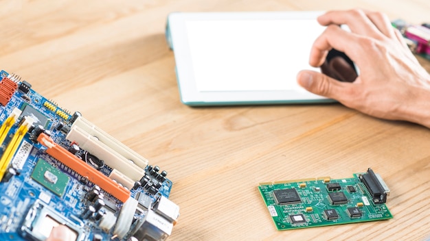 Free photo close-up of hand touching digital tablet with motherboard and circuit on wooden table