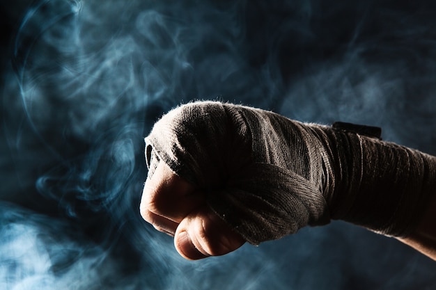 Free photo close-up hand with bandage of muscular man training kickboxing  on black and blue smoke