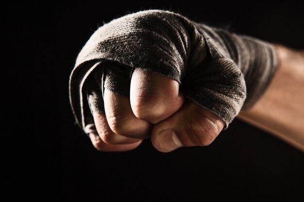 Close-up hand with bandage of muscular man training kickboxing  on black