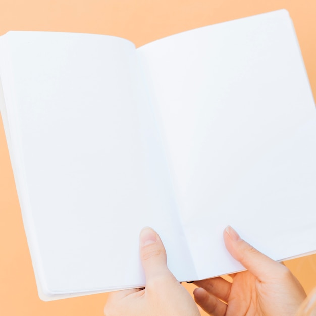 Free Photo close-up of hands holding blank white book against colored backdrop