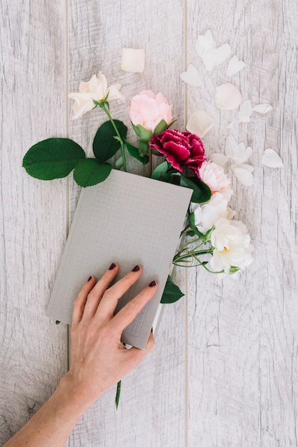 Free Photo close-up of hands holding diary with flowers on wooden table